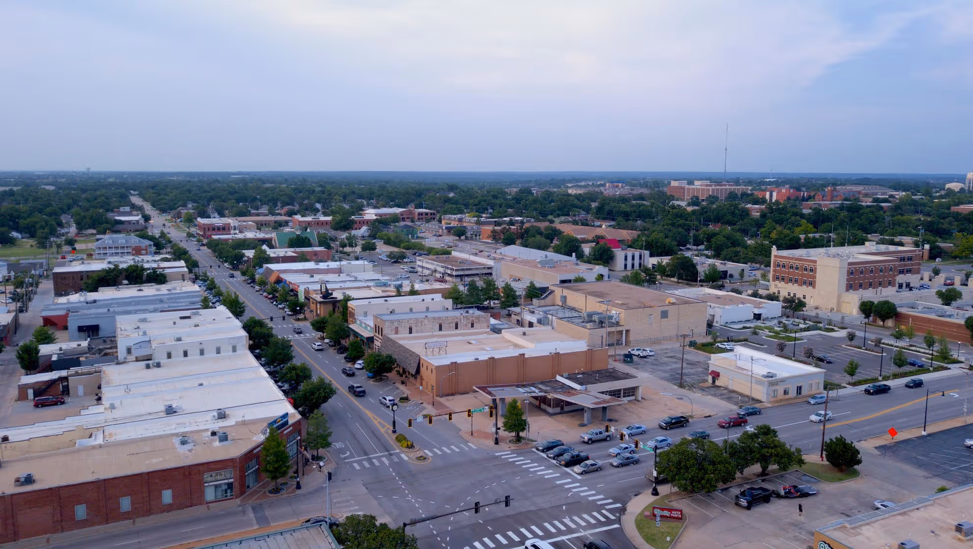 Aerial view of downtown Edmond showing streets lined with low-rise commercial buildings, parking lots, and greenery extending to the horizon.