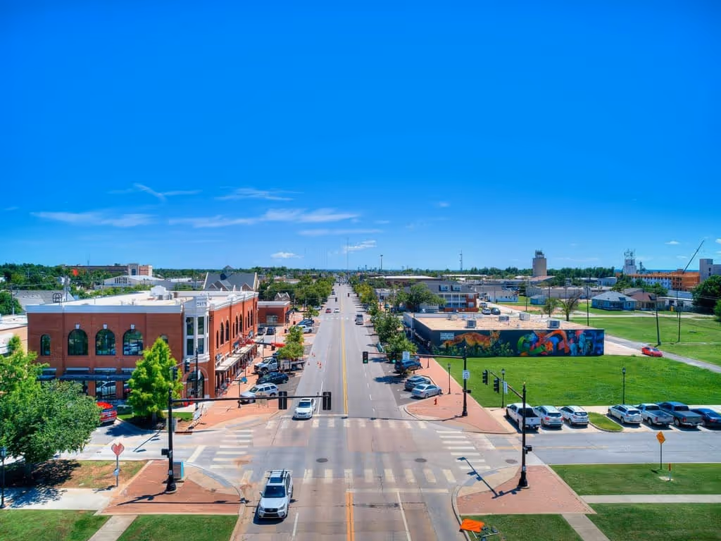 Aerial view of a small-town main street with brick buildings, parked cars, a colorful mural, and a clear blue sky.