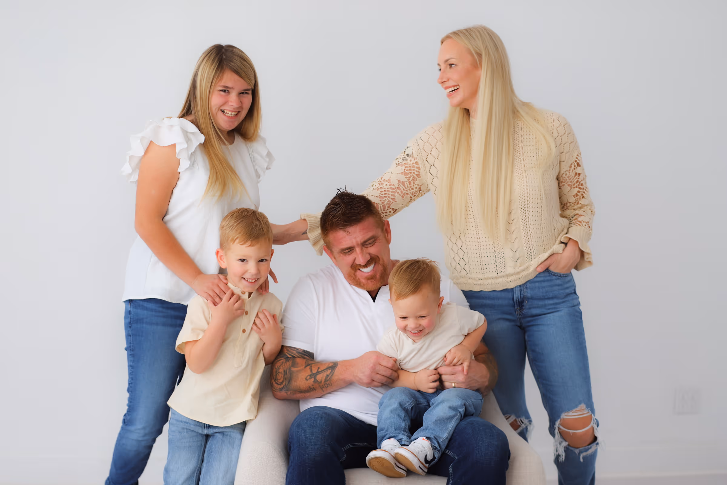 Group portrait of Roofing by Prodigy owners Matthew Maloy, Nicholas Mullaney and their families, standing together against a white background, all wearing casual white and light-colored tops with blue jeans.