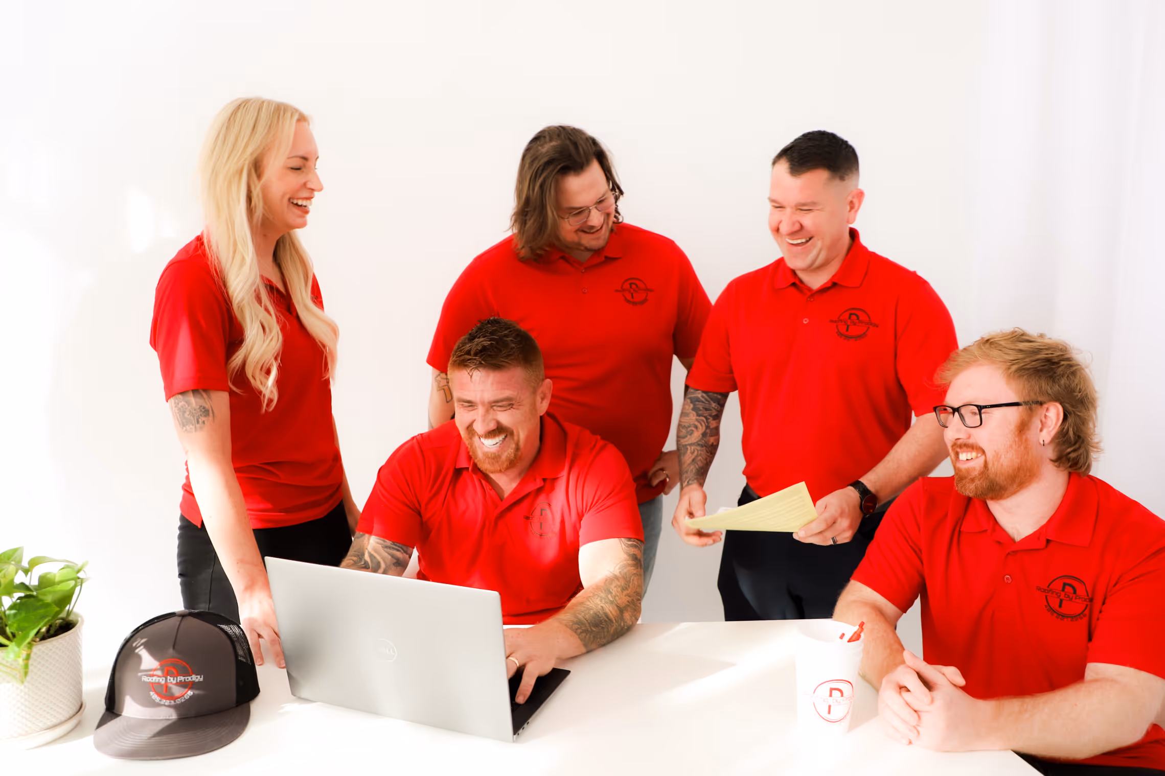 The Prodigy Restoration team in matching red polo shirts gathered around a laptop in a bright room.