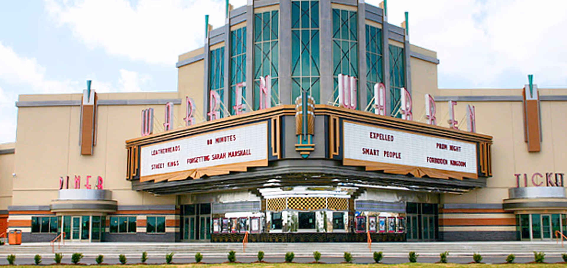 Art deco style movie theater marquee with green tinted windows and titles of several films displayed.