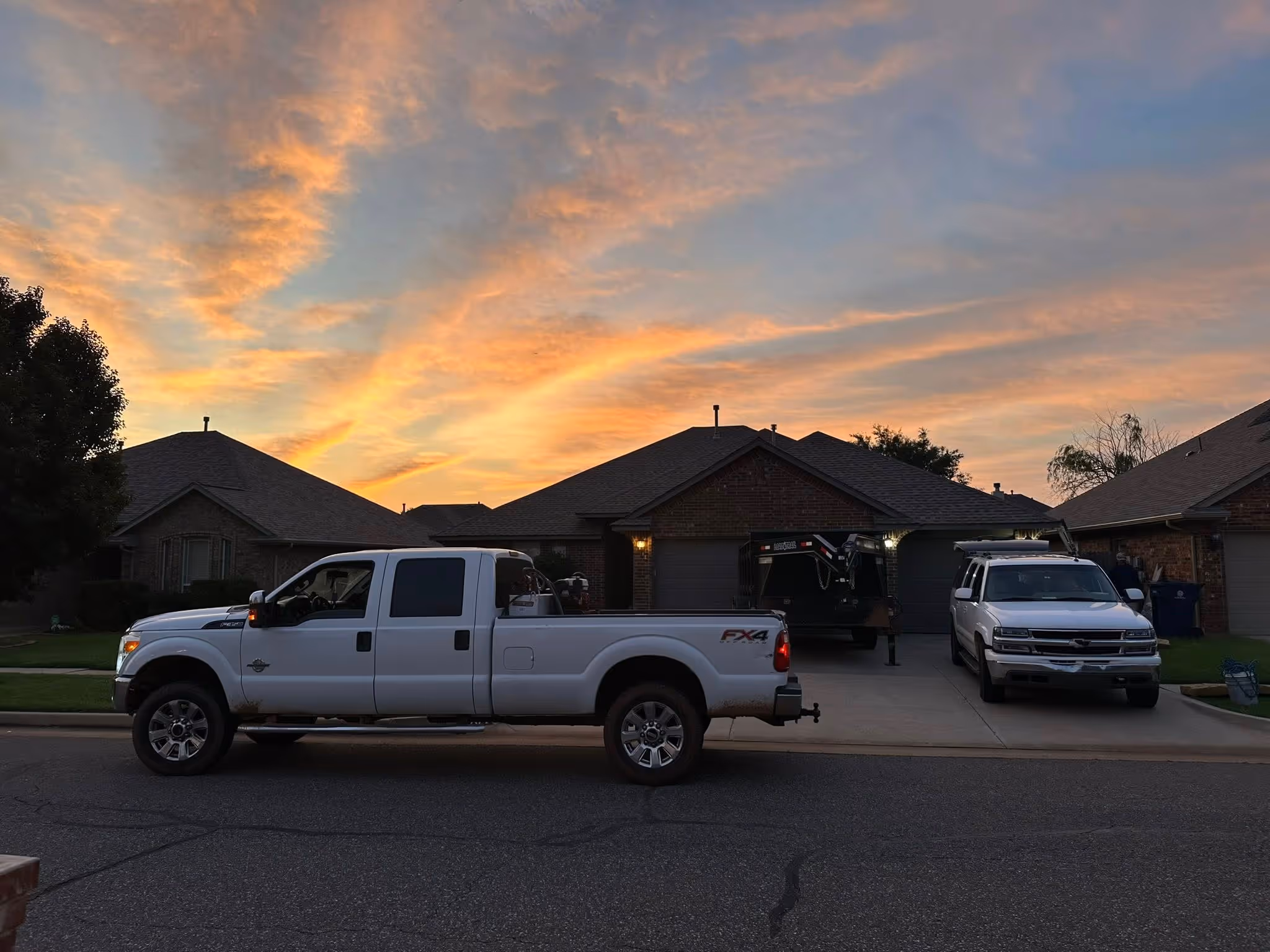 Roofing by Prodigy - White pickup truck parked on street in front of suburban houses at sunset with colorful clouds.