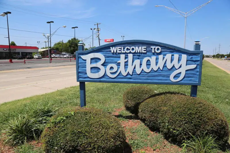 Blue wooden sign with white letters reading 'Welcome to Bethany' placed on grassy area beside a road.