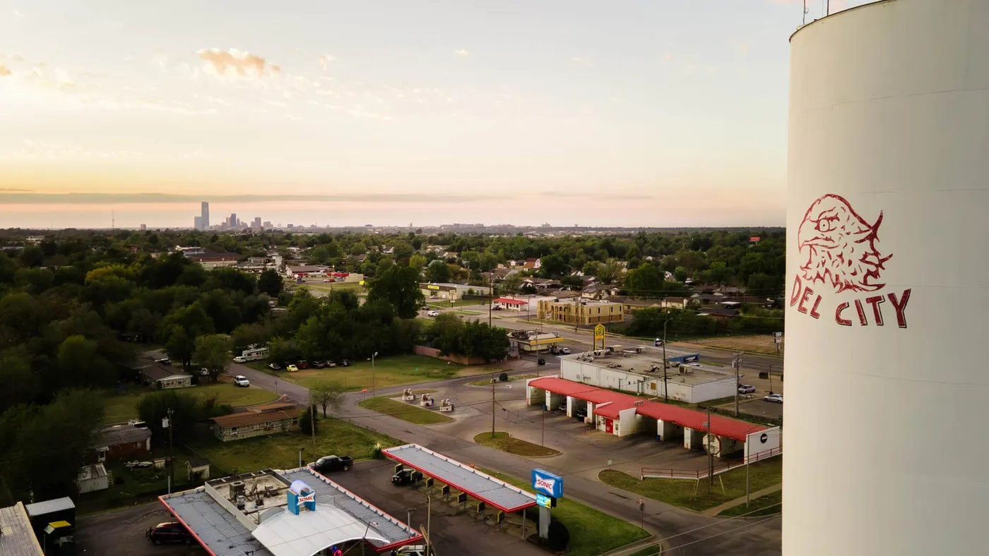 Aerial view of Del City businesses and tree-lined streets with the Oklahoma City skyline on the horizon.