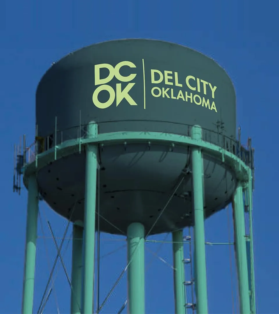 Green Del City water tower painted with the "DC OK, Del City Oklahoma" logo against a blue sky.