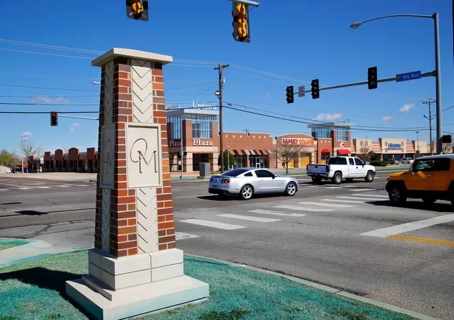 Brick "MC" monument at a busy Midwest City intersection lined with shops and restaurants.
