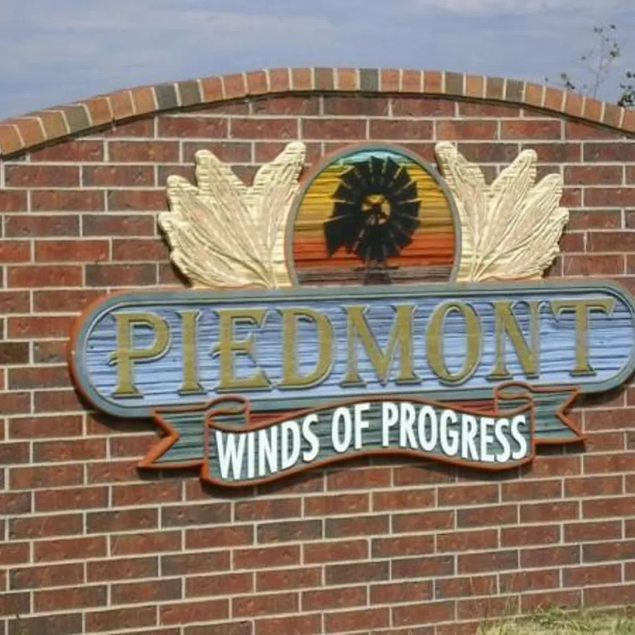 Brick "Piedmont, Winds of Progress" welcome sign with a sunflower emblem in Piedmont, Oklahoma.