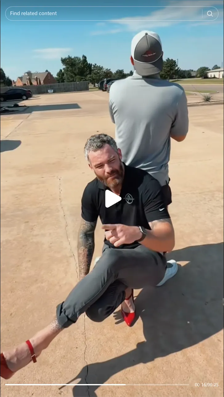 Roofing by Prodigy - A man with tattoos wearing red high heels crouches on a sunlit concrete surface beside another man standing with his back turned, outdoors on a clear day.