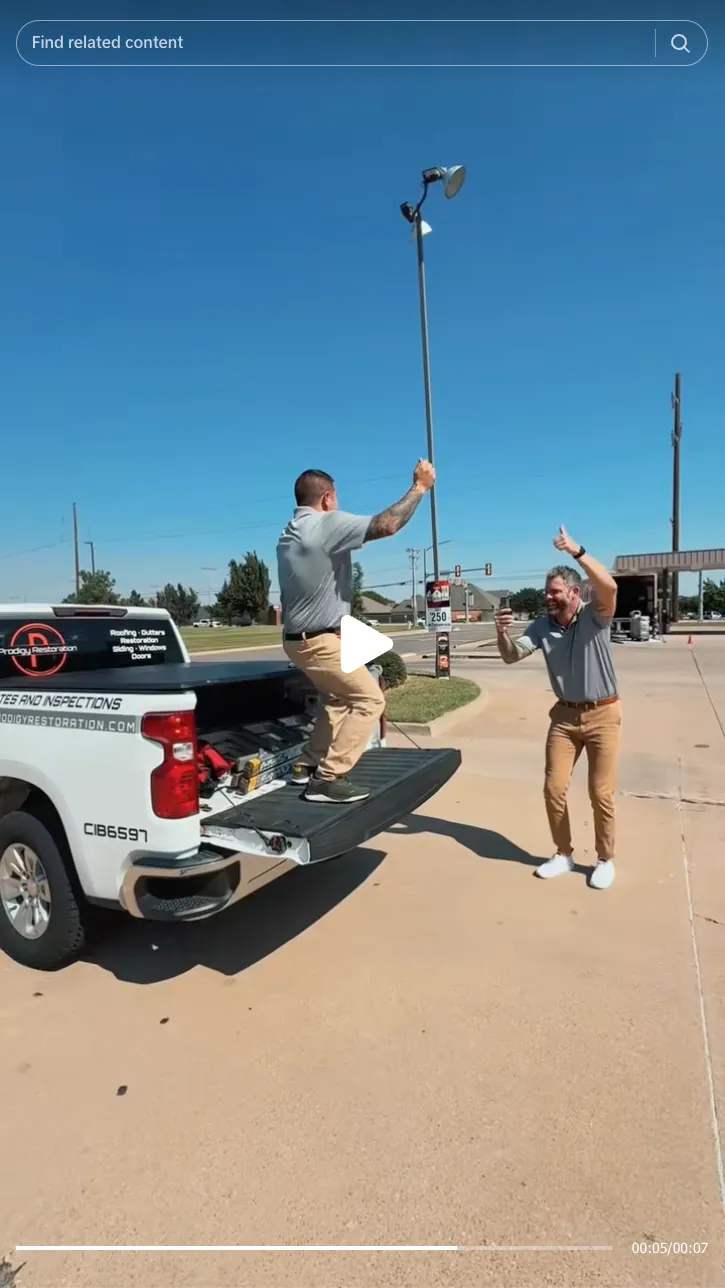 Roofing by Prodigy - Two men in gray shirts and tan pants celebrate near a white pickup truck with the tailgate down in a sunny parking lot.