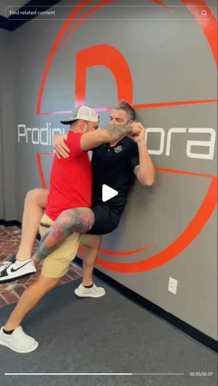Roofing by Prodigy - Two men practicing a physical lift or wrestling move indoors near a wall with Prodigy logo.