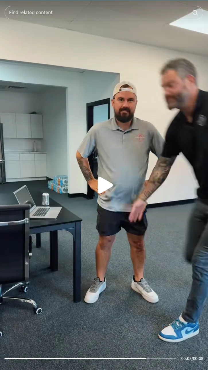 Roofing by Prodigy - Two men in a modern office; one stands still looking at the camera wearing a gray polo, shorts, and a backwards cap, the other is blurred mid-motion wearing a black shirt and blue sneakers.
