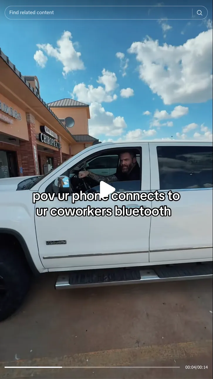 Roofing by Prodigy - A man with tattoos sits in the driver's seat of a white pickup truck parked outside a chiropractic office under a partly cloudy blue sky.
