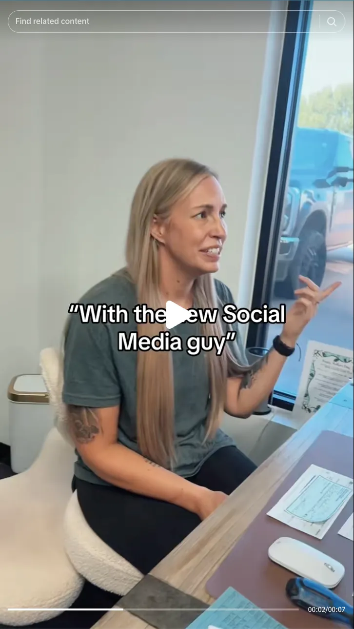 Roofing by Prodigy - A woman with long blonde hair and tattoos on her arms sits in an office chair by a desk, gesturing with her hand during a conversation with text overlay 'With the new Social Media guy'.