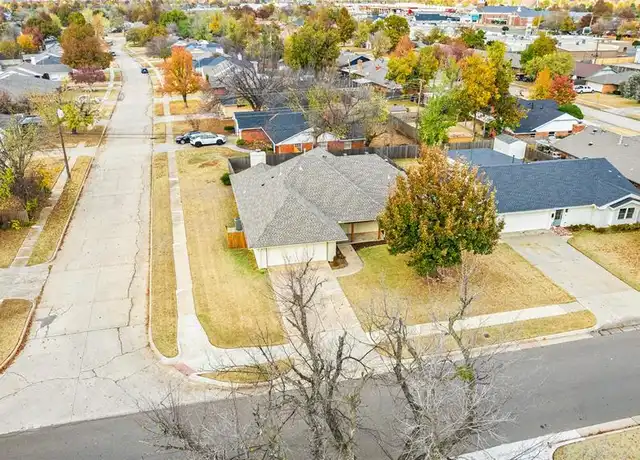 Aerial view of a suburban neighborhood with houses, trees with autumn foliage, sidewalks, and empty streets.